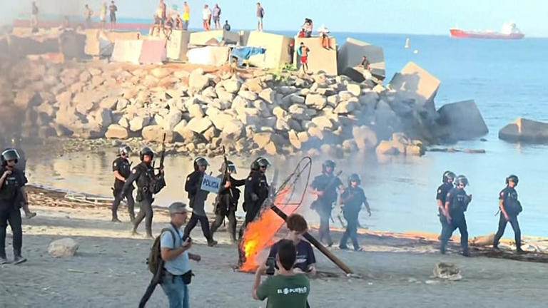Police take up position as protesters set fire to objects on a beach where migrants had been sheltering in Ceuta.