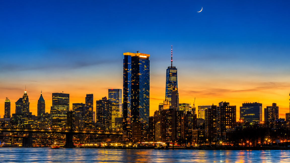 New York City glows beneath a crescent moon at dusk