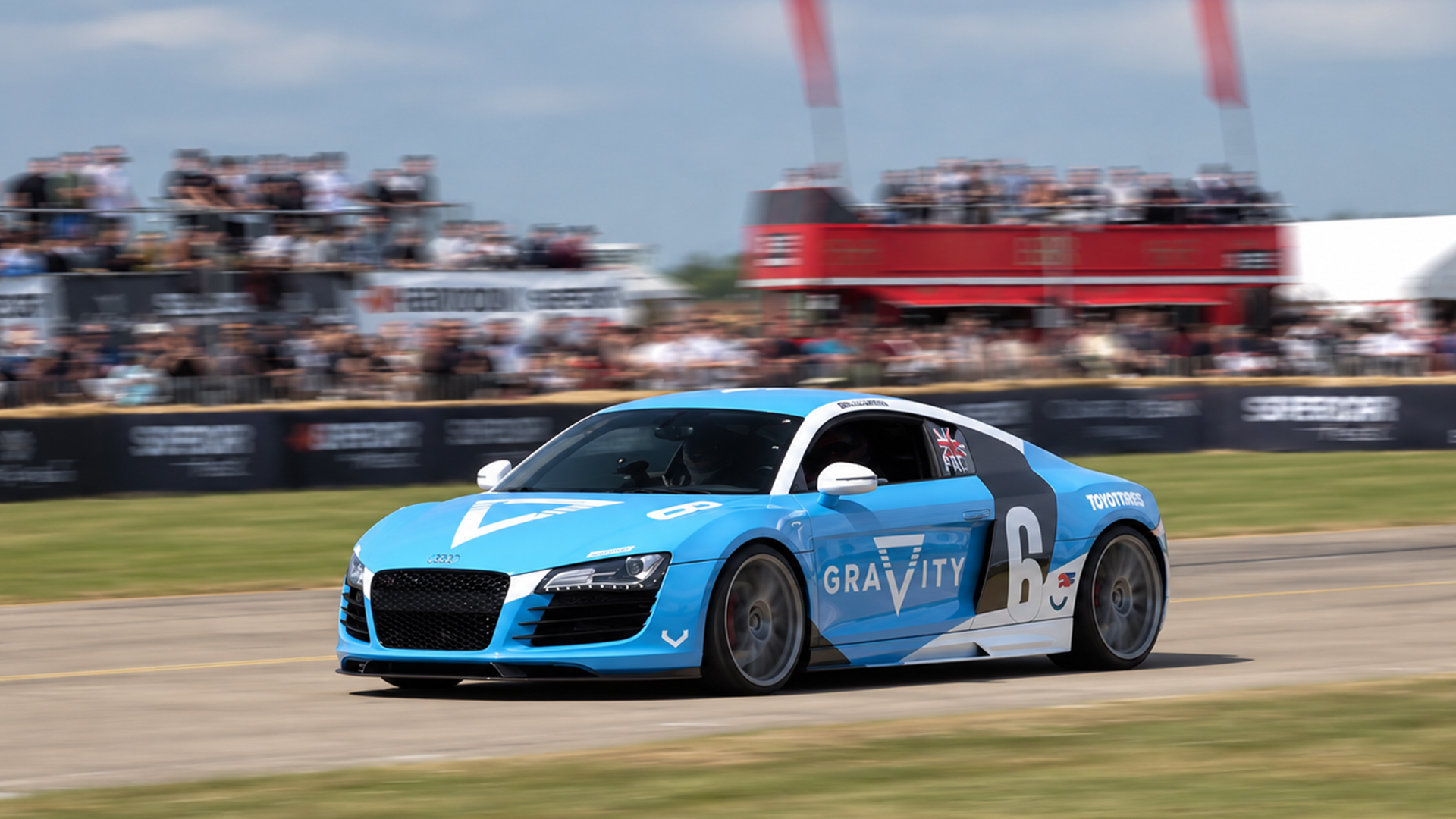 Audi R8 races past a packed grandstand in bright livery