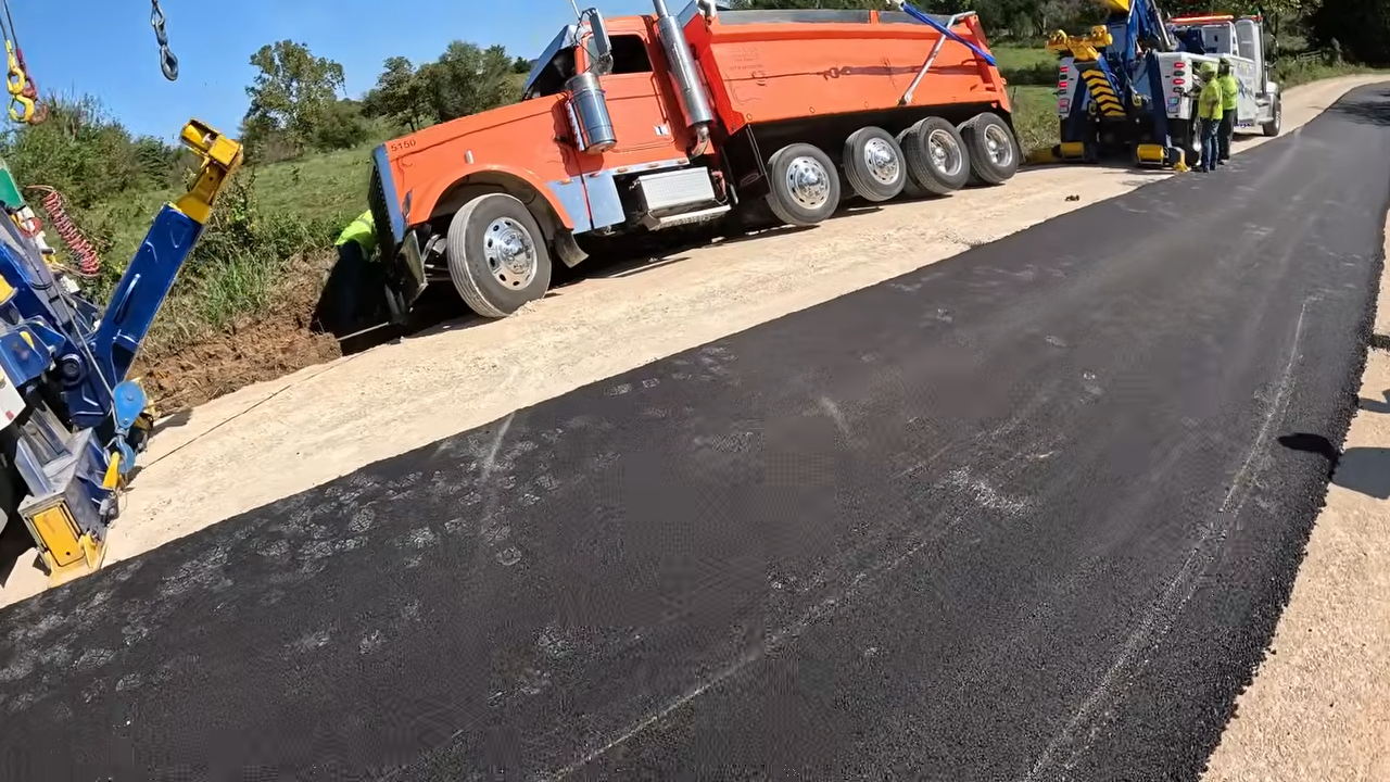 Dump truck loaded with hot asphalt slides off the road