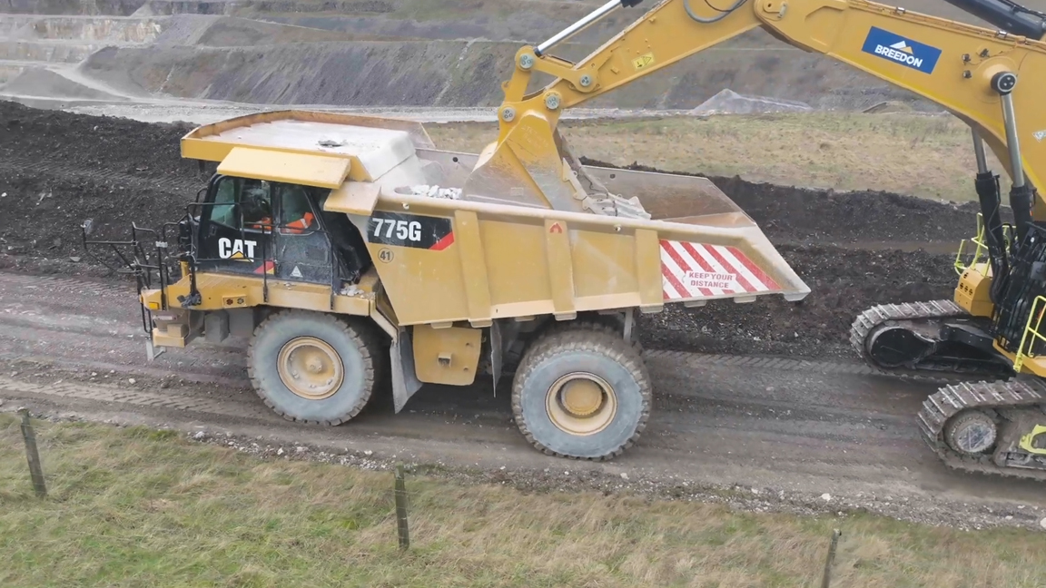 Giant excavator loads heavy haul truck in an open pit quarry
