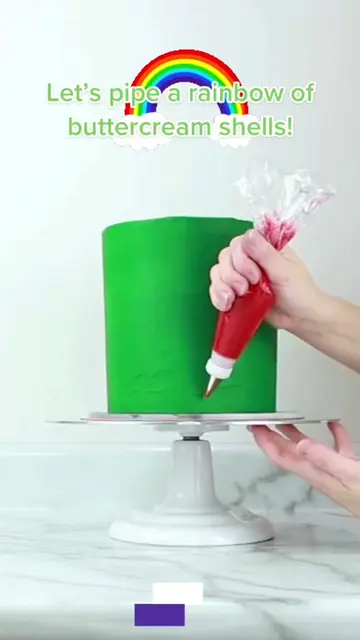 Piping a rainbow buttercream border on a tall green cake