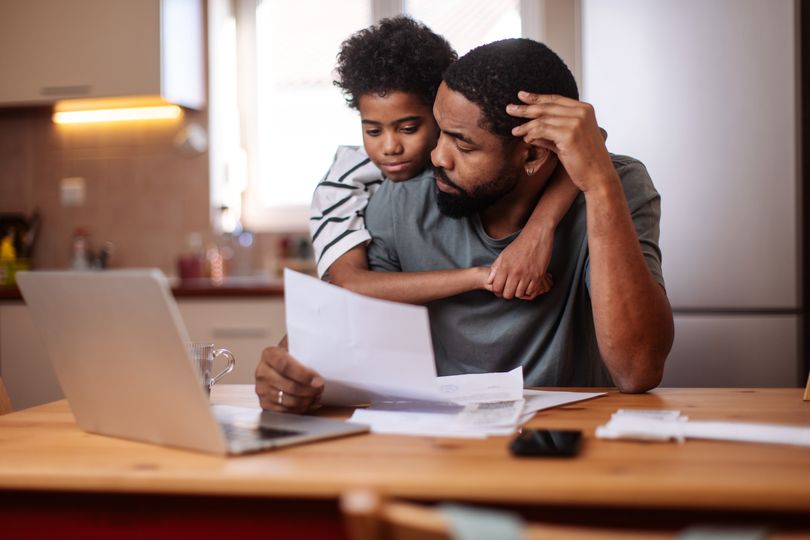 Father and son bond at the kitchen table while reviewing bills and using a laptop together.