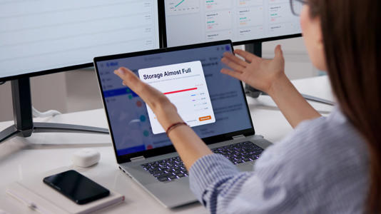A woman looking at a storage alert on her laptop, holding her hands out in frustration and disbelief