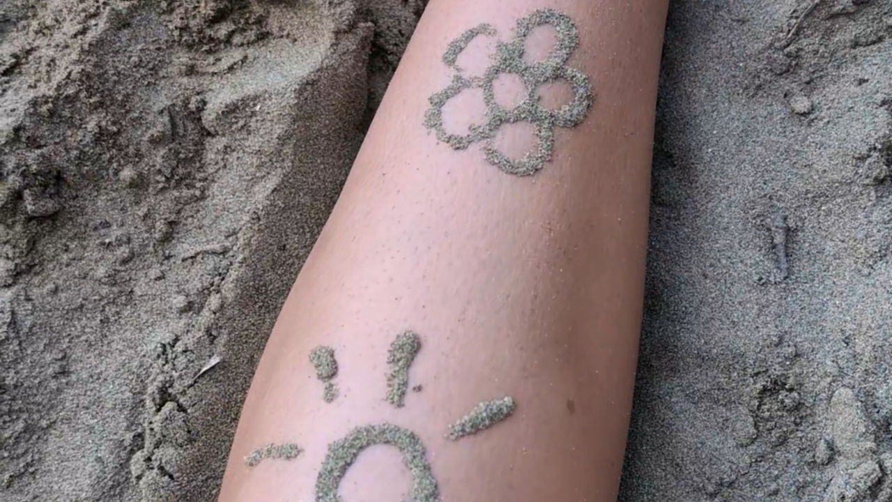 Woman applies fine sand to create a leg tattoo