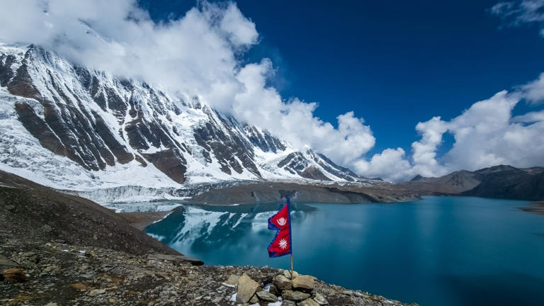 Bandera de Nepal en el lago Tilicho, con las montañas del Himalaya y los glaciares al fondo.