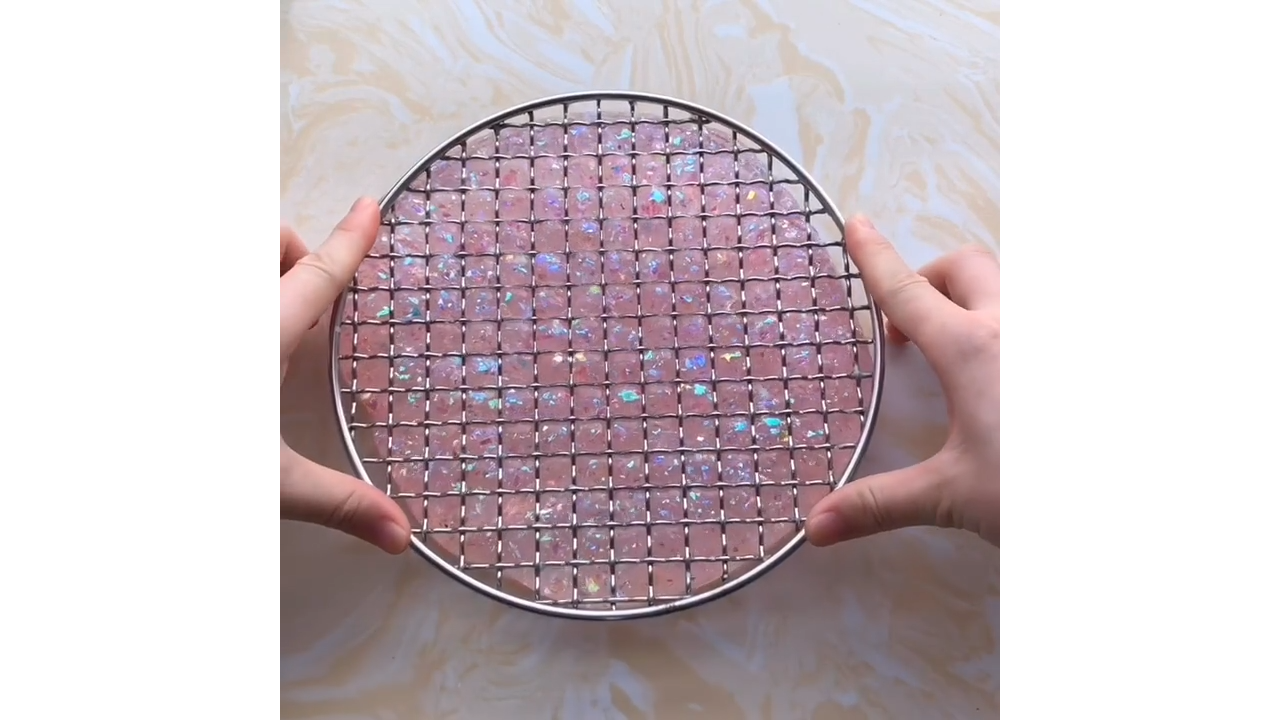 Pressing pink glitter slime through grid creating satisfying square pops