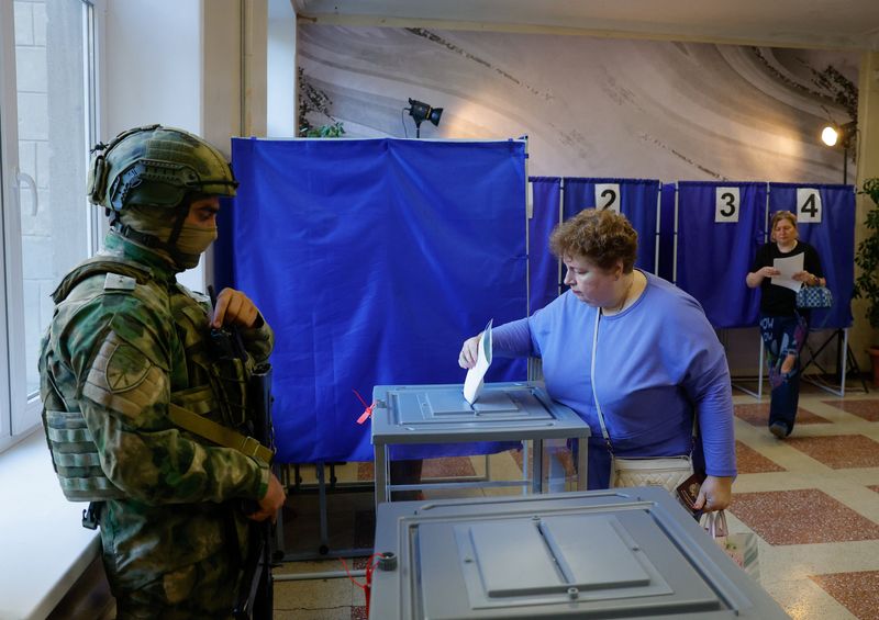 A woman casts her ballot next to a serviceman securing a poling station during Russia's parliamentary elections, in the course of Russia-Ukraine conflict in Donetsk, Russian-controlled Ukraine, September 18, 2026. REUTERS/Alexander Ermochenko