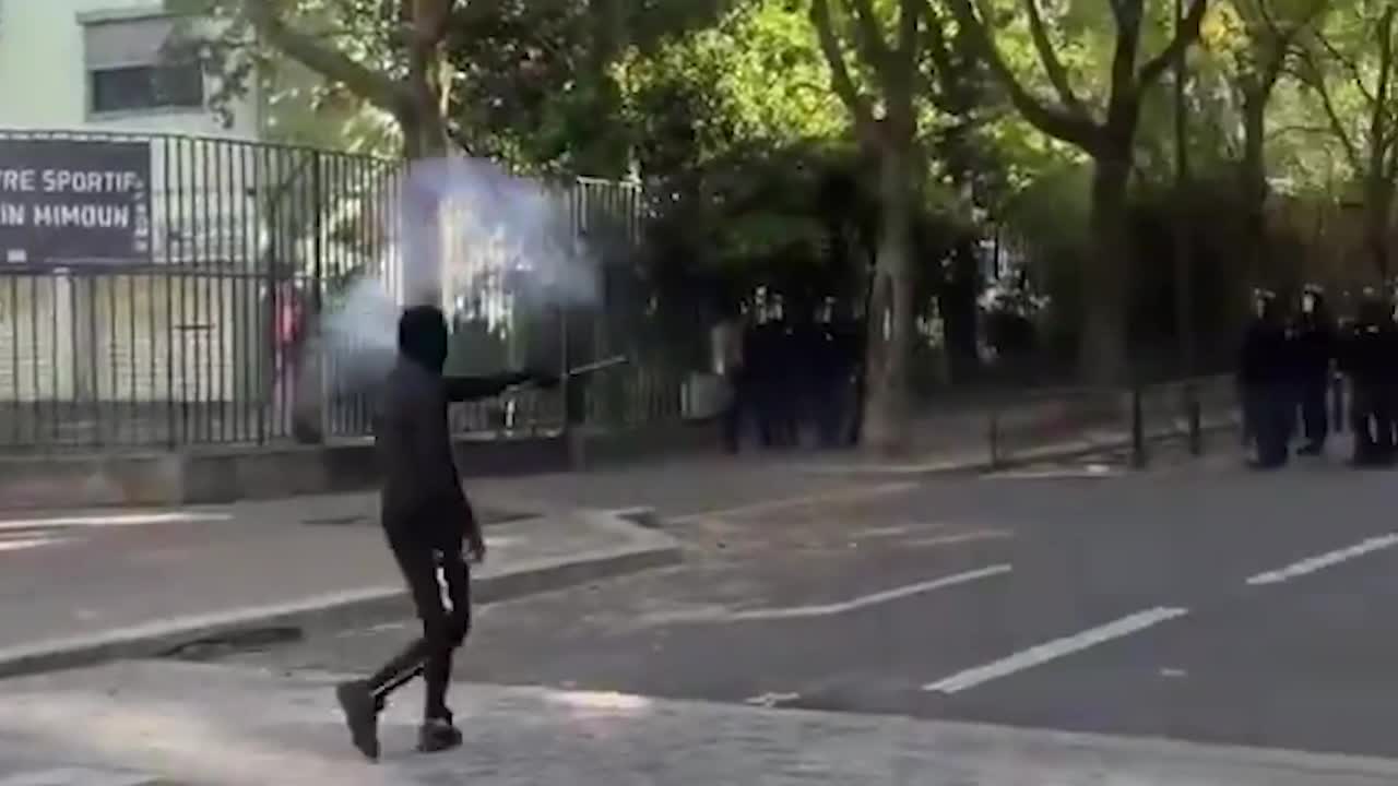 Masked figure fires firework at large group of riot cops who then ...