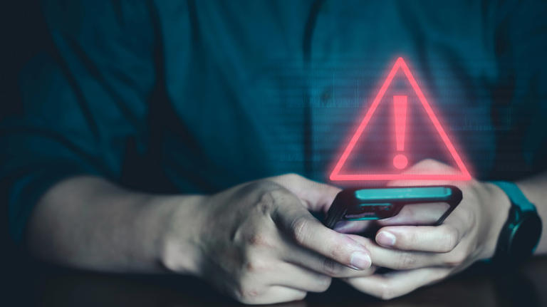 Person using smartphone with a red warning sign overlaid above it.