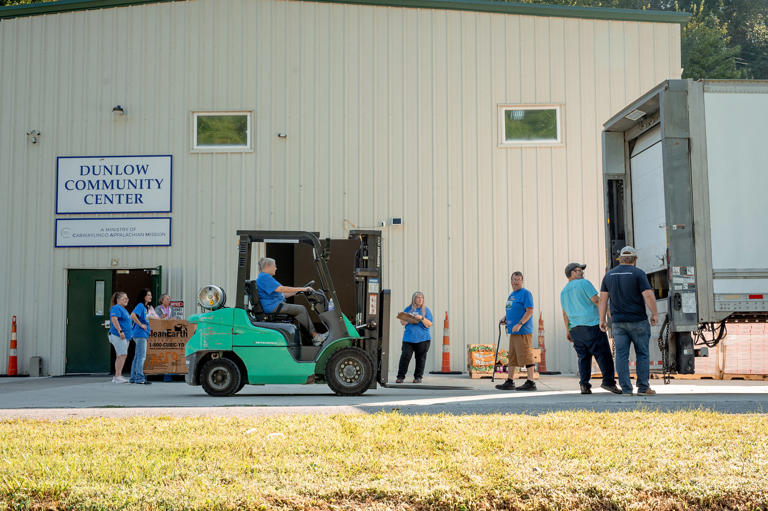 A longtime staff member operates the forklift to unload food, most of it purchased by Facing Hunger Foodbank. Bill Likens, center right, directed the food into position for the waiting cars. (Mike Belleme for NBC News)