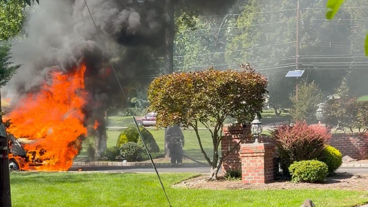 Flames engulf a van while firefighters move in