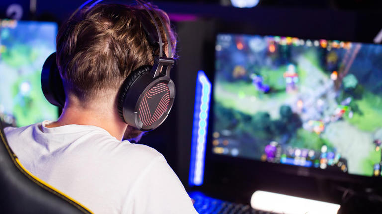 Person wearing a gaming headset while playing on a desktop PC with multiple monitors.