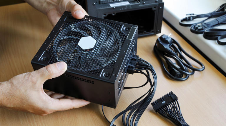 Person holding a modular PC power supply with cables on a desk.
