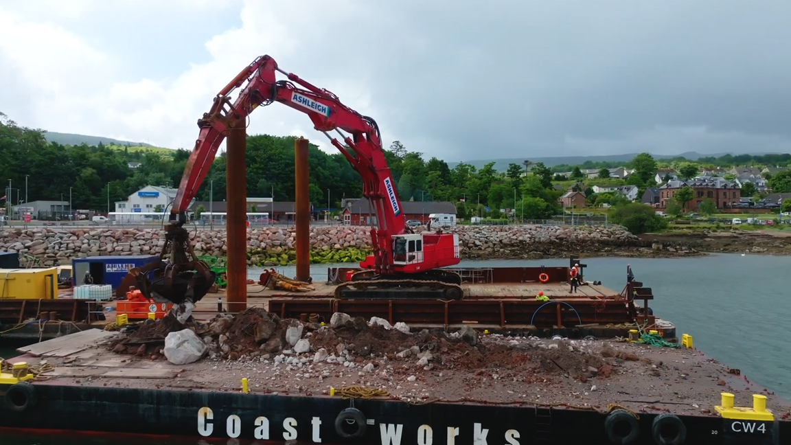 Powerful excavator lifting massive rocks from a floating construction barge
