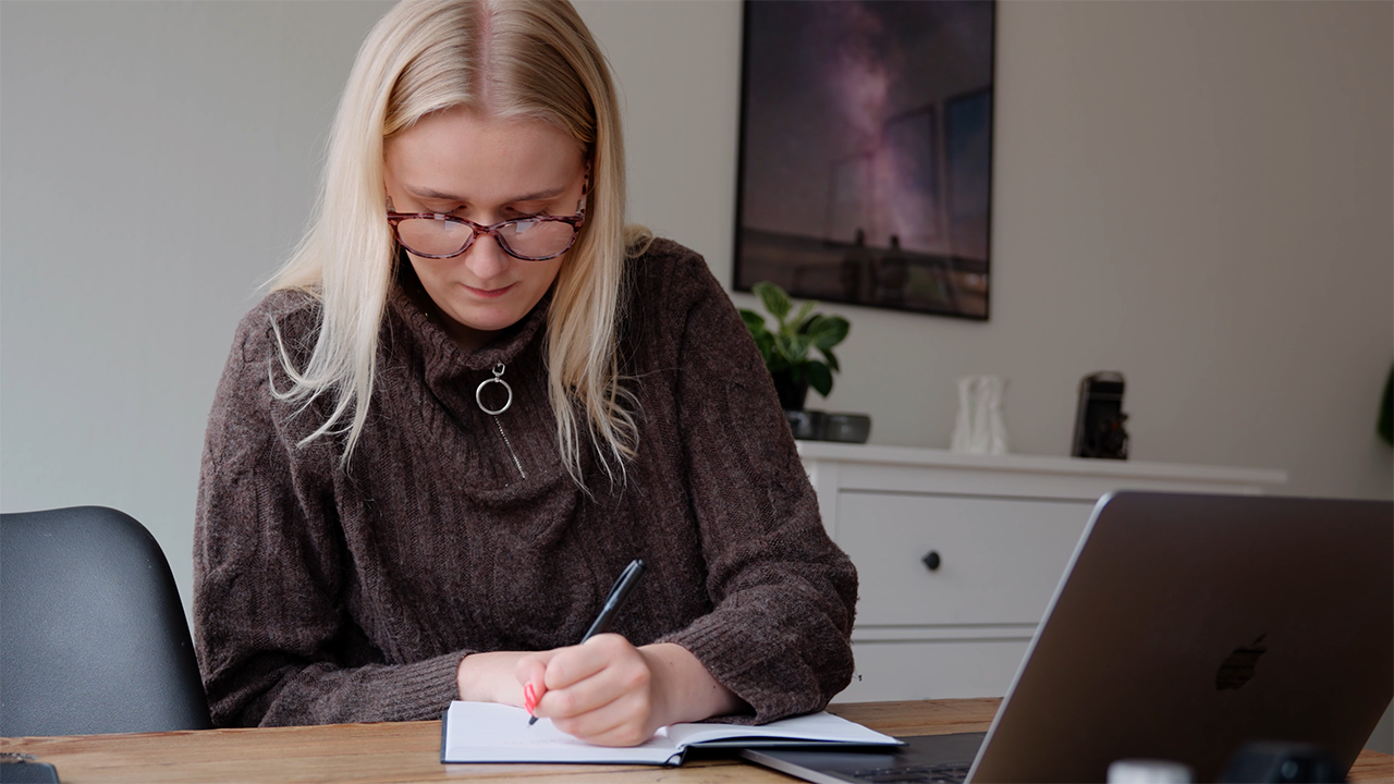 Writing notes in a notebook while working on a laptop