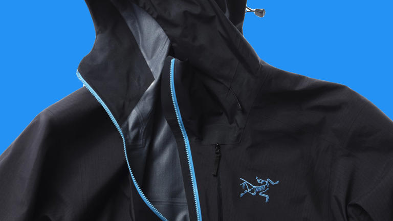 Black hooded jacket featuring a light blue zipper and a blue embroidered chest logo, shown on a solid bright blue background.