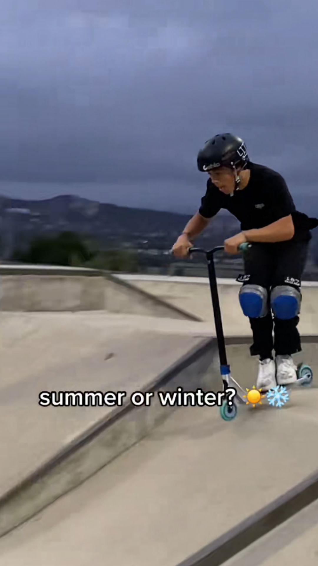 Scooter rider cruises past ramps and rails at the skatepark