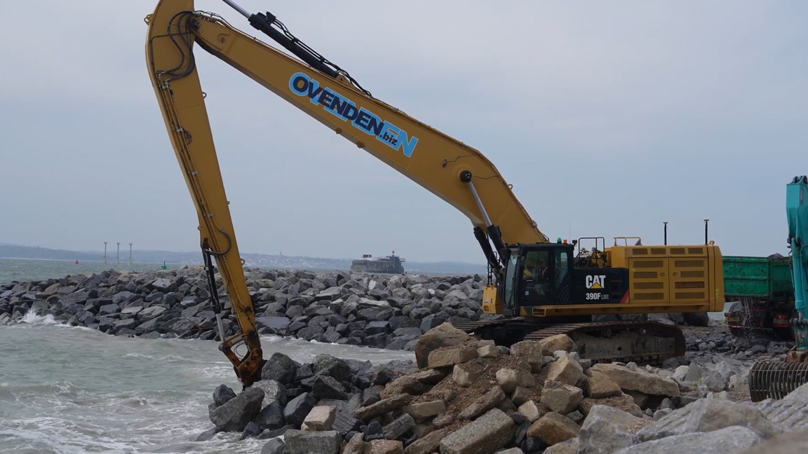 Giant hydraulic excavator positioning heavy boulders in ocean waves