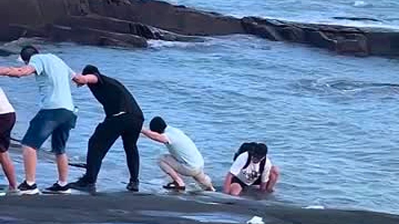 Tourists form human chain to pull man stranded on slippery sea rocks to ...