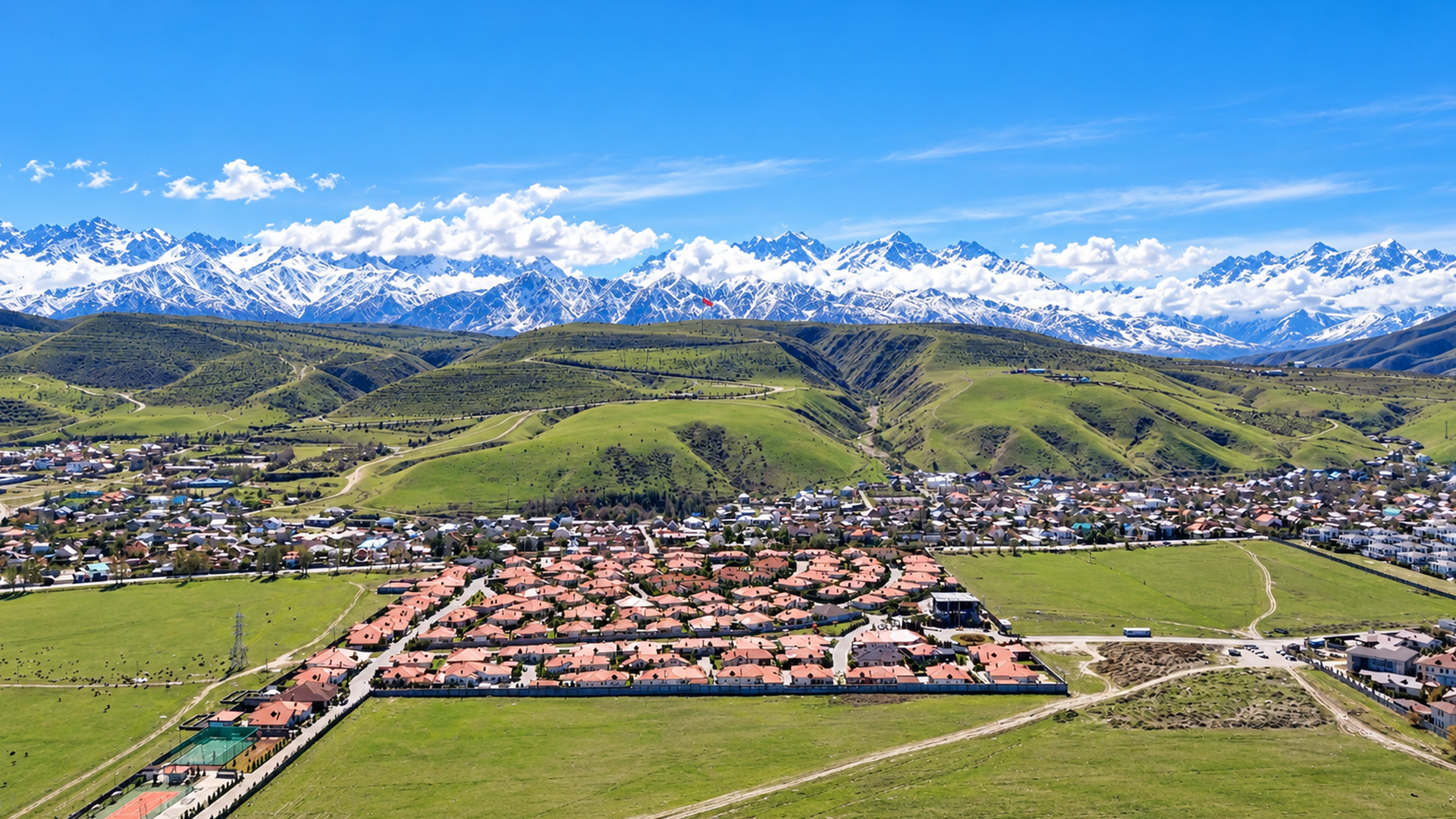 A city surrounded by green hills and snowy mountains