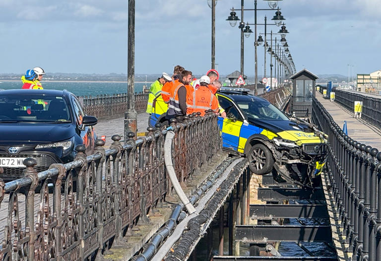 Police car dangling precariously off seaside pier in crash trapping two ...