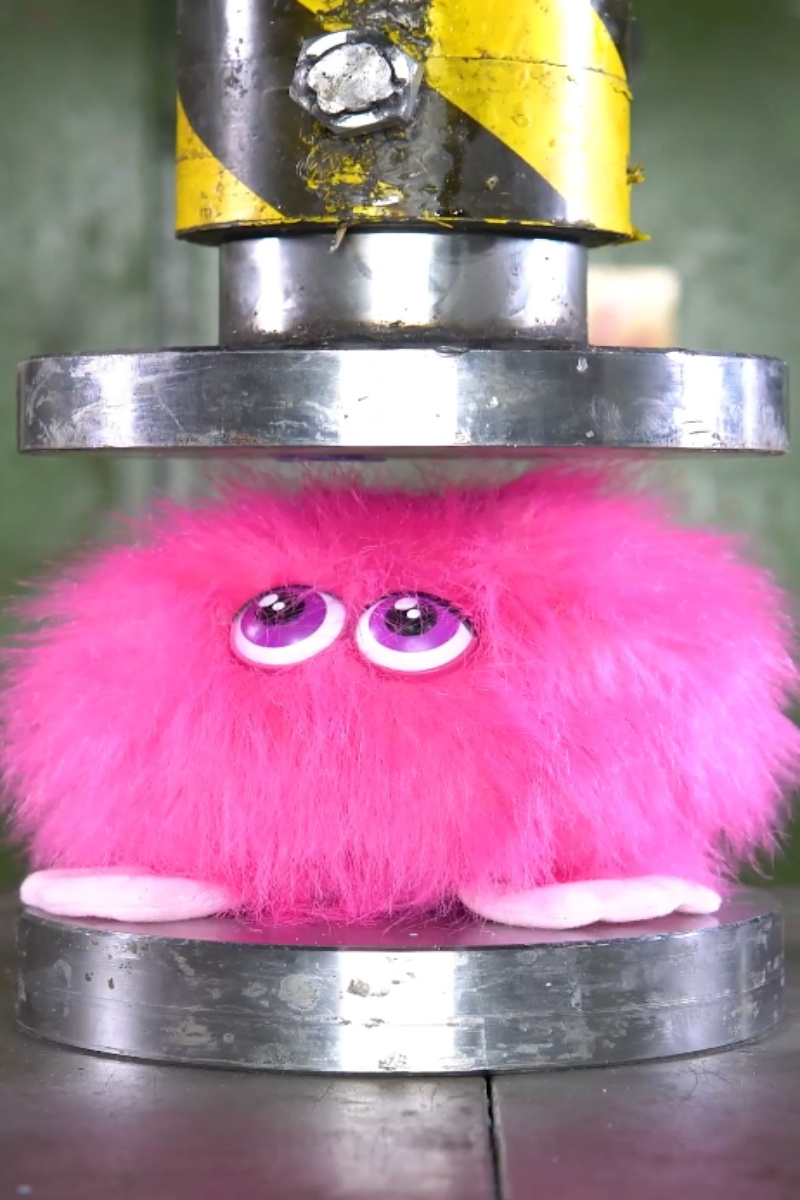 Brinquedo de peluche cor-de-rosa esmagado por uma prensa hidráulica