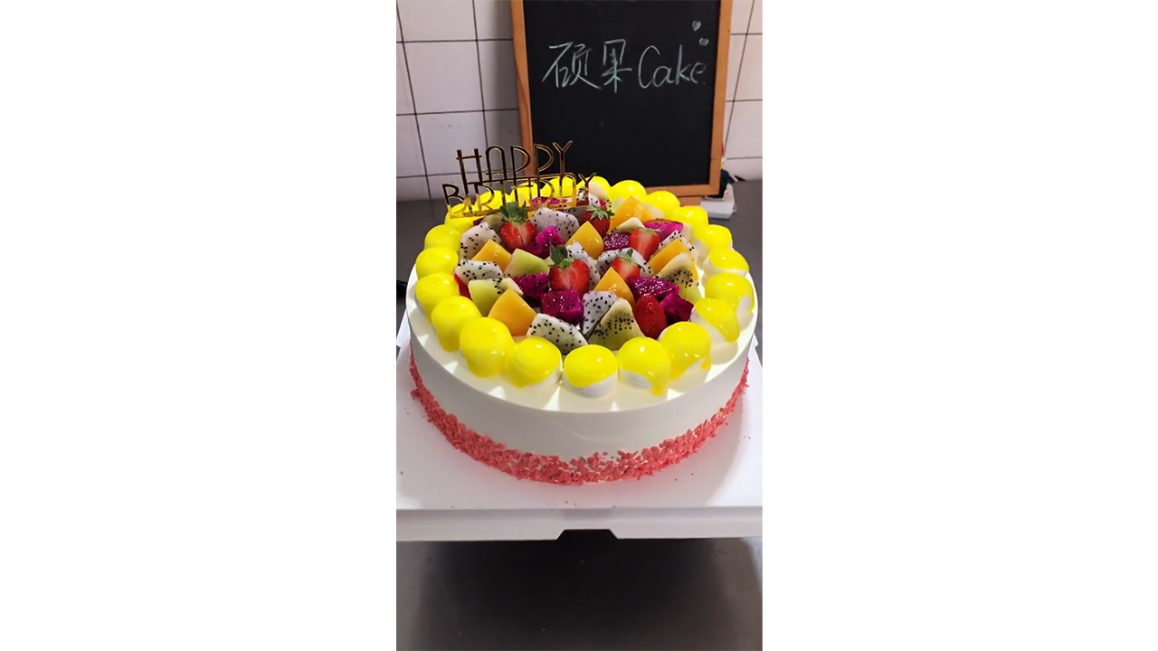 Decorating white birthday cake with yellow cream drops and tropical fruits
