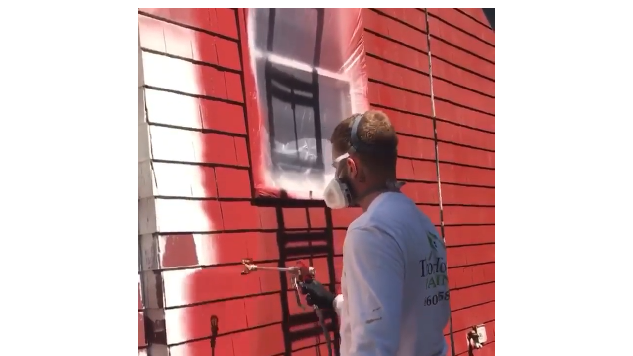 Spray painting wooden house siding with bright red coating creating ...