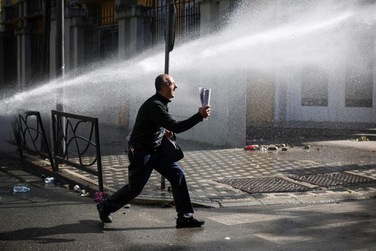 A demonstrator screams toward police positions amid a stream of water from a water cannon near the Ministry of Education during an anti-government protest by students in Tirana, Albania, October 16, 2026. REUTERS/Louisa Gouliamaki