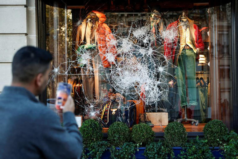A man takes photos of a vandalised Ralph Lauren storefront a day after clashes during a national day of demonstrations against the cost of living and rising fuel prices, in Paris, France, October 18, 2026. REUTERS/Benoit Tessier