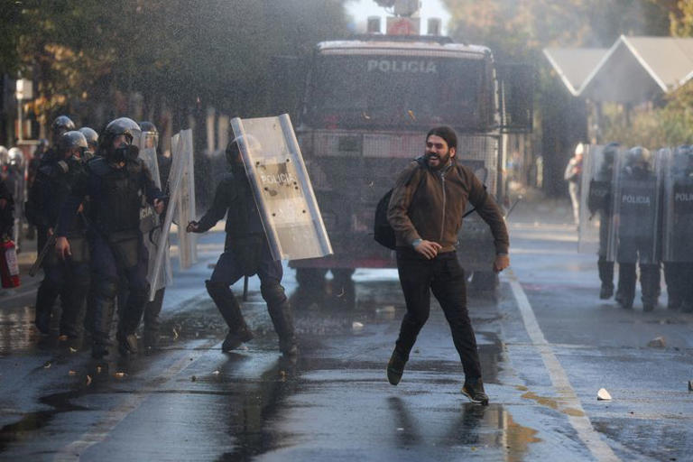 A man runs next to police in riot gear, during an anti-government protest by students in Tirana, Albania, October 18, 2026. REUTERS/Louisa Gouliamaki