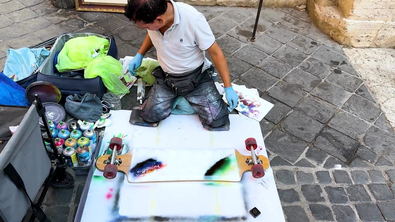 A Rome street artist spray paints over a skateboard’s owl design