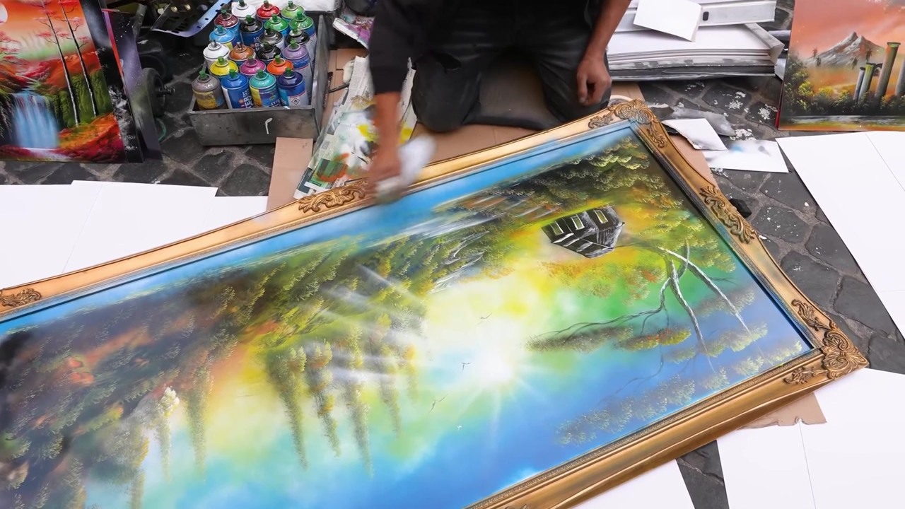 Street artist spray paints a landscape on a mirror