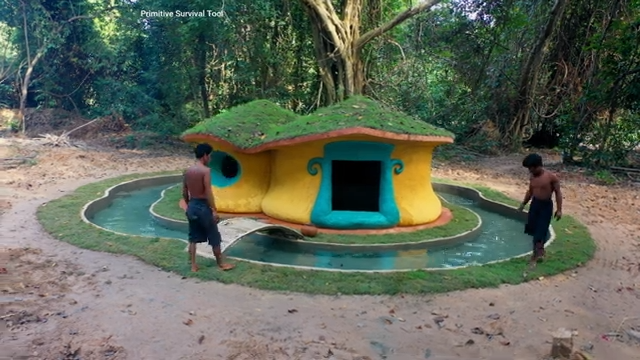 Builders reinforce a fish pond beside a hobbit-style house