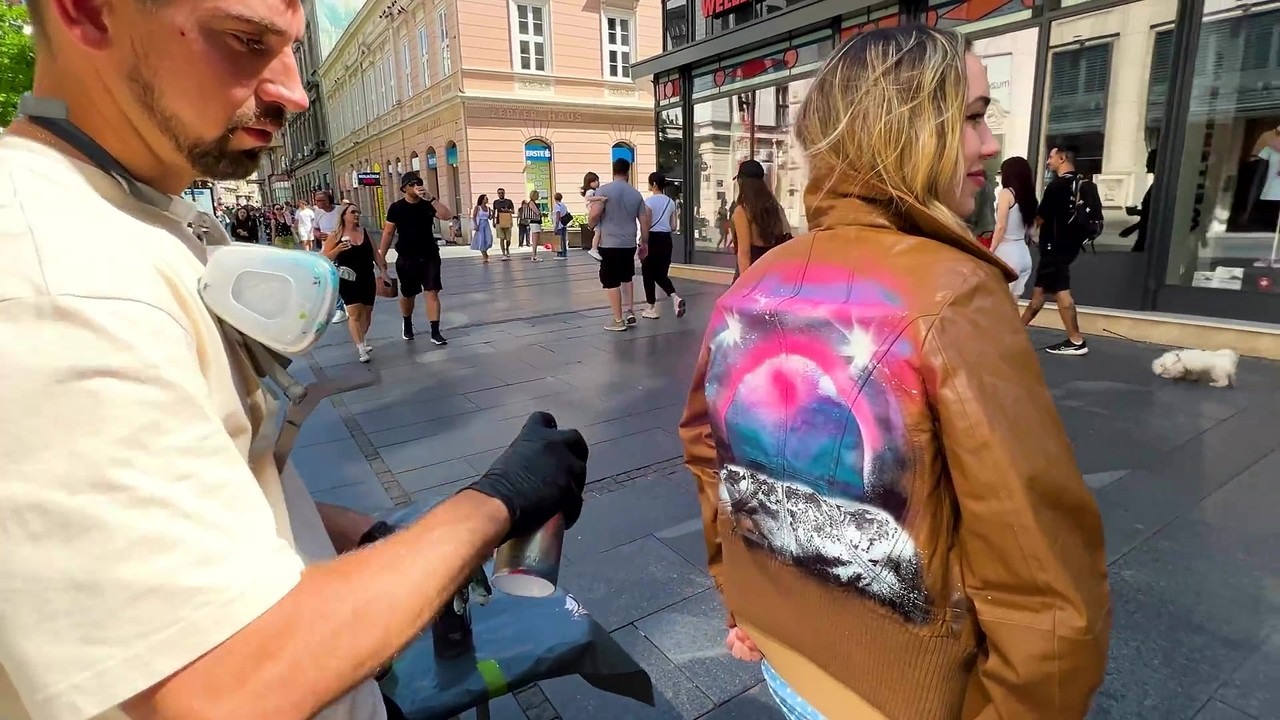 A street artist spray paints a stranger’s new jacket in public