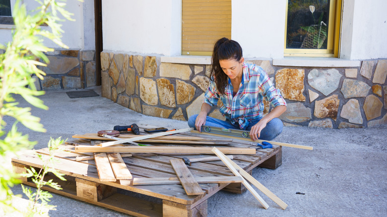 Woman replaces concrete slabs with old wood pallets for a DIY deck with ...
