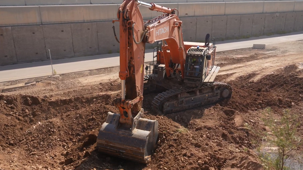 Heavy crawler excavator digging deep into rocky soil at a construction site