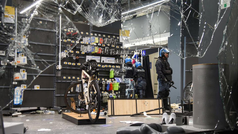 Police officers stand inside a looted Decathlon sporting goods store behind shattered glass in Milan, Italy, on Sunday. - Stringer/Reuters