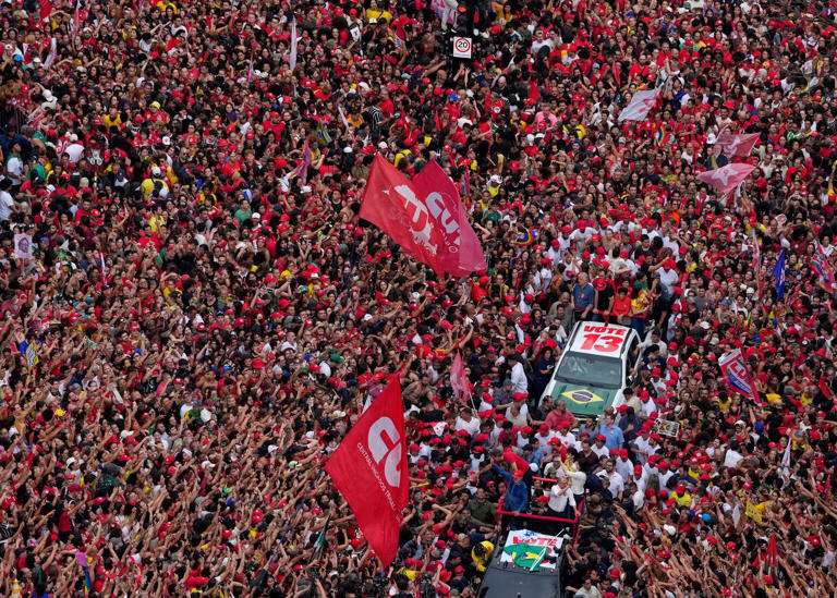 Brazilian President Luiz Inacio Lula da Silva, wearing a red cap and blue shirt, waves to supporters from the front of a vehicle during his final campaign rally (Andre Penner/AP)