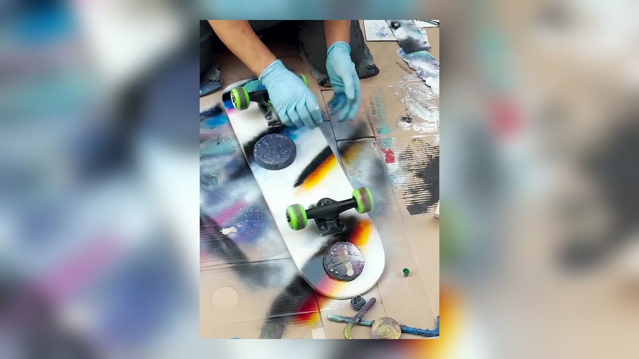 Street artist spray paints a plain skateboard deck