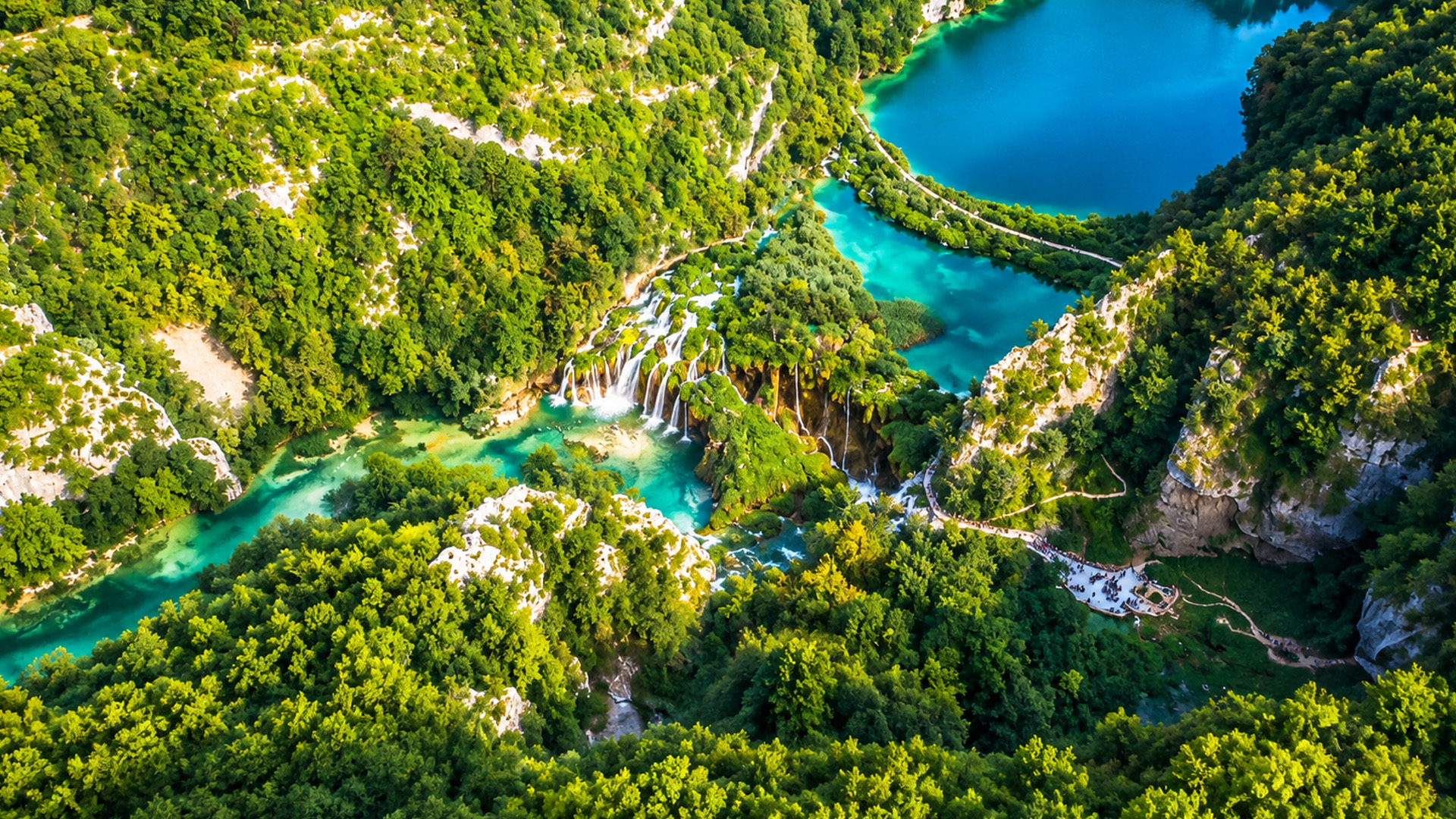 Hidden waterfalls flow between bright blue forest lakes