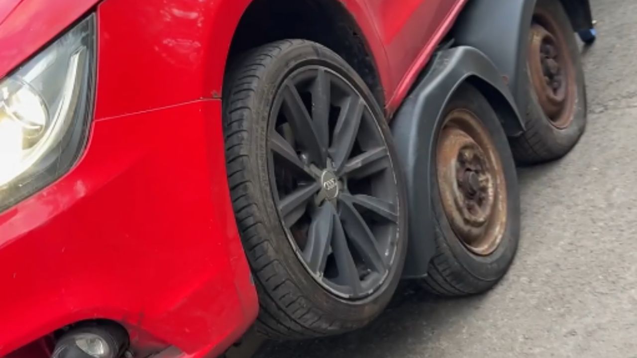Shocking car mishap as red vehicle perches on trailer wheel arch