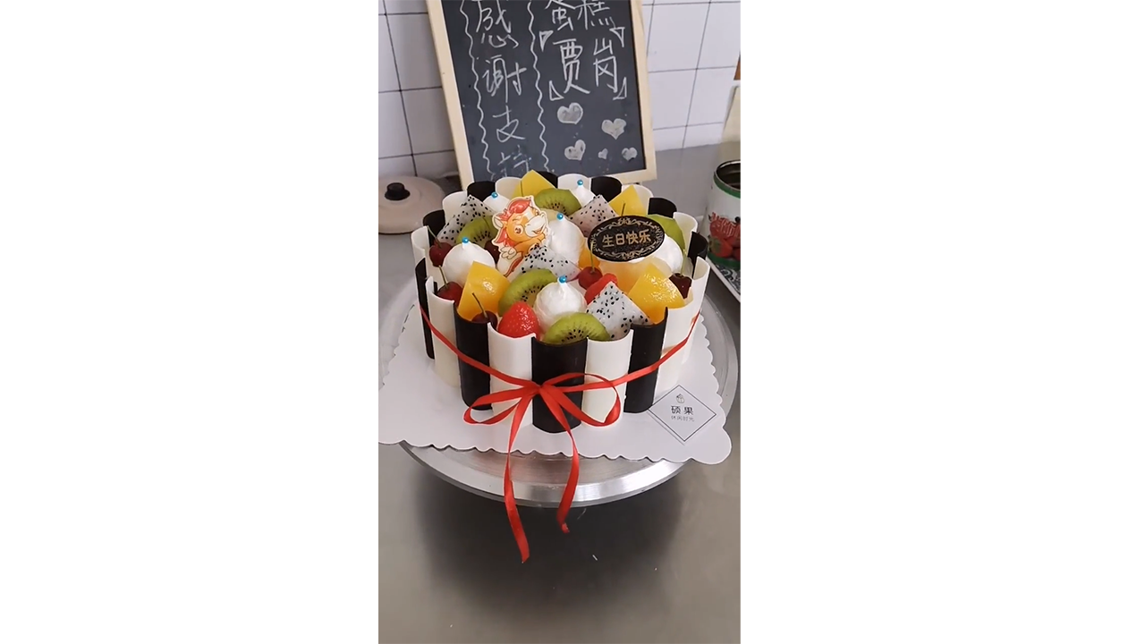 Decorating tropical fruit cake with black chocolate panels and red ribbon
