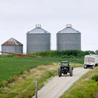 File photo a farmer drives his tractor past a soybean field toward grain storage bins near Ladora, Iowa.