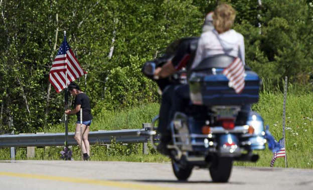 In this June 22, 2019 file photo, a motorcycle passes as a woman leaves flowers at the scene of an accident on Route 2 in Randolph, N.H., where seven motorcyclists were killed in a crash the day before.