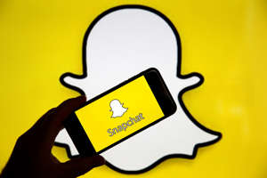 PARIS, FRANCE - APRIL 05: In this photo iIllustration, the Snapchat social media logo is displayed on the screen of an iPhone in front of a computer screen showing a Snapchat logo on April 05, 2019 in Paris, France. During its 'Partner Summit 2019' in Santa Monica, Snapchat has announced several new features to come. Most notable is the ability to send stories to the Tinder dating app. Snapchat is a free photo and video sharing application which has 13 million daily users worldwide. (Photo by Chesnot/Getty Images)