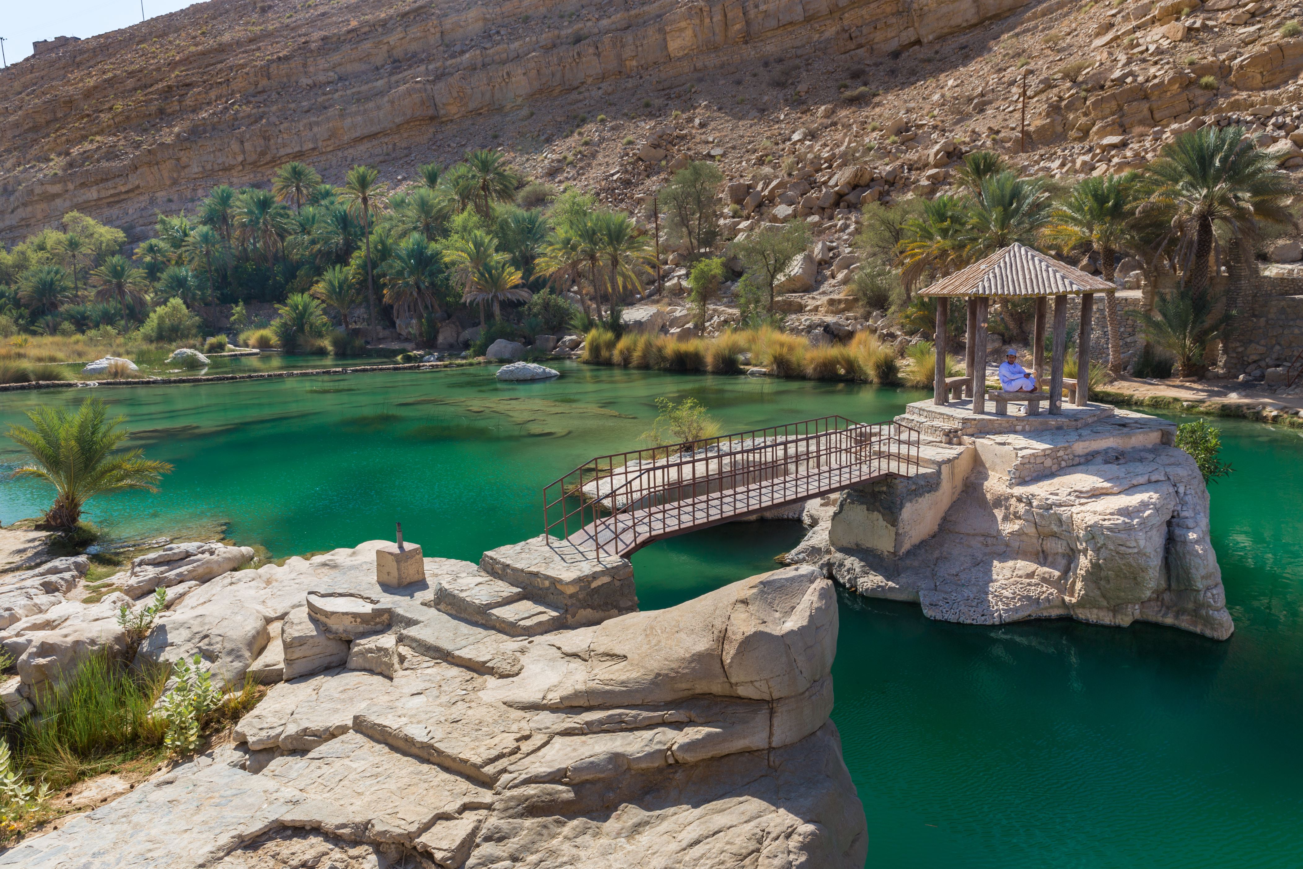 ����� 3 �� 16: WADI BANI KHALID, OMAN - NOVEMBER 26, 2017: A man relaxes at the amazing view of the emerald pools in Wadi Bani Khalid, Oman
