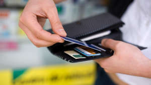 a hand holding a cell phone: Close-up of a woman getting a credit card out of her wallet.