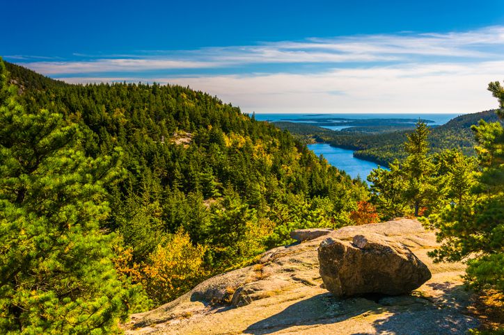 Slide 14 of 29: The different types of terrain and variations in the landscape are some of the incredible sights available at Acadia National Park. This view from North Bubble shows a veritable Whitman’s Sampler of Acadia attractions – the woods, the water, and the landmasses in the distance.